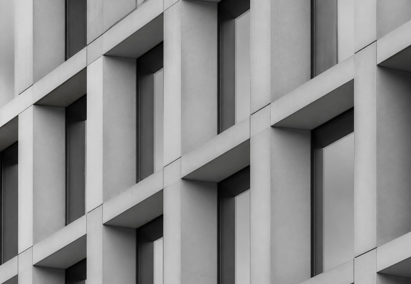 Grayscale detail of a repeating concrete facade with deep window recesses, photographed at an angle
